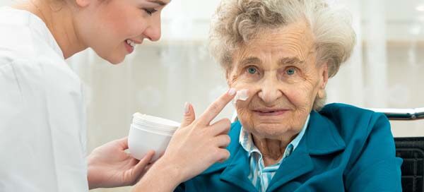 Elderly woman with a nurse applying face cream.