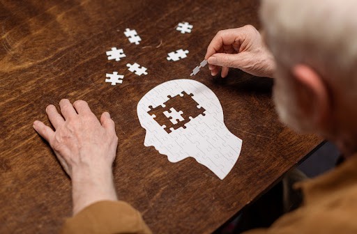 A senior man putting a puzzle together; the puzzle resembles a head with pieces missing