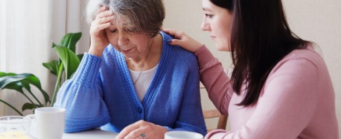 A daughter with her hand on her senior mother's shoulder showing concern and empathy due to her mothers symptoms of Alzheimer’s